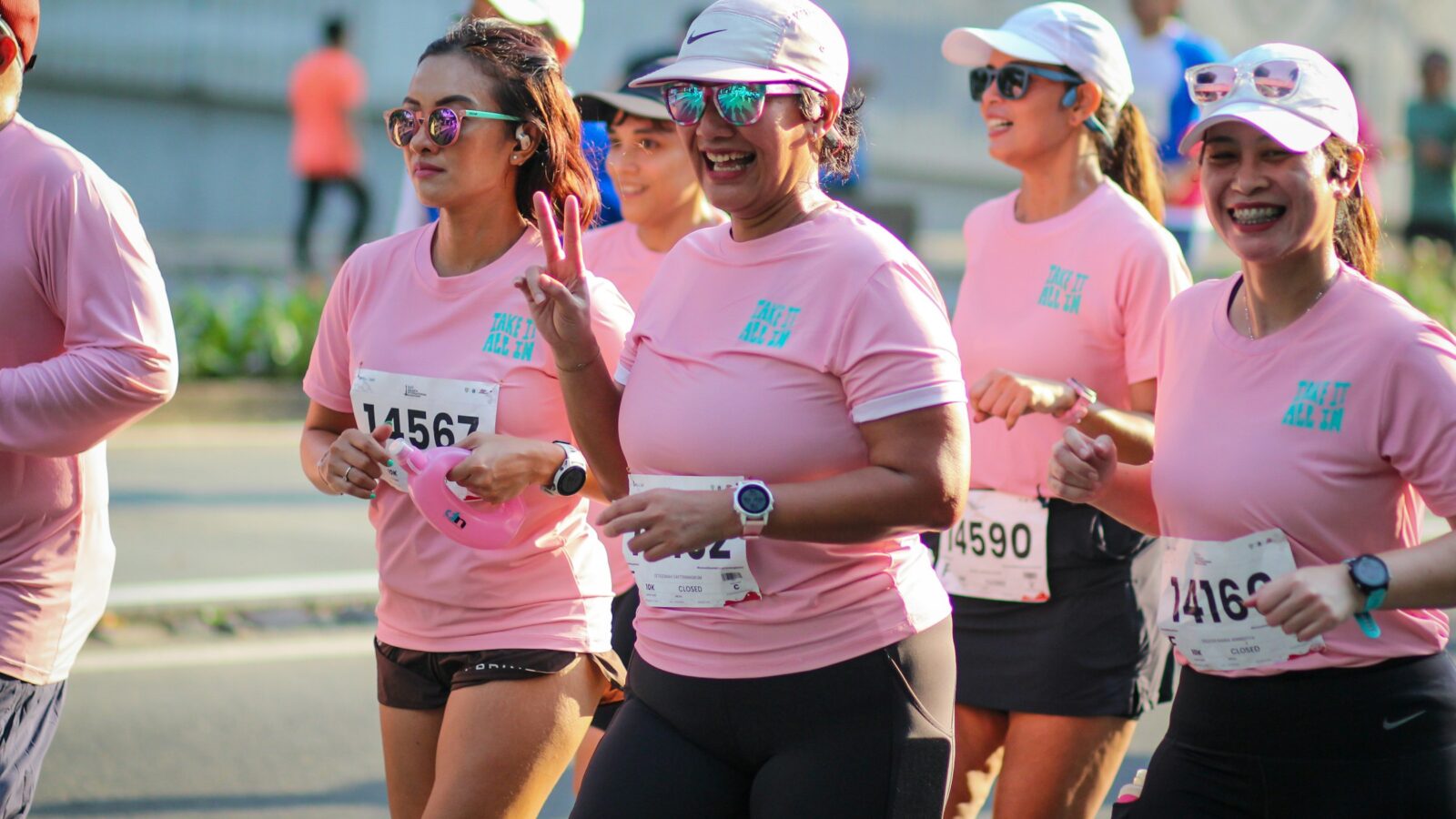 Women in pink shirts smiling as they run a race together
