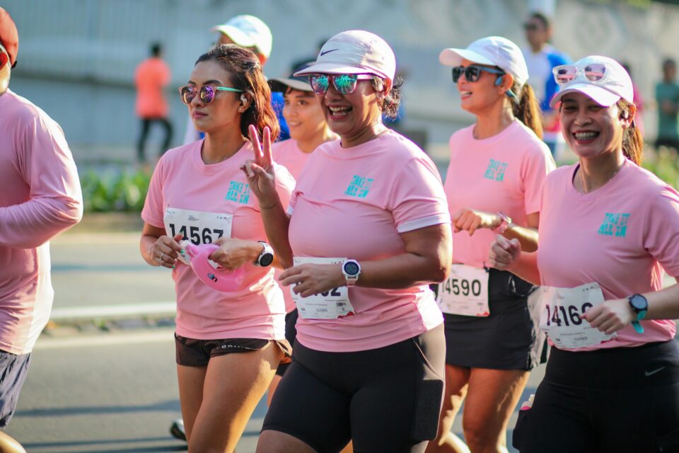 Women in pink shirts smiling as they run a race together